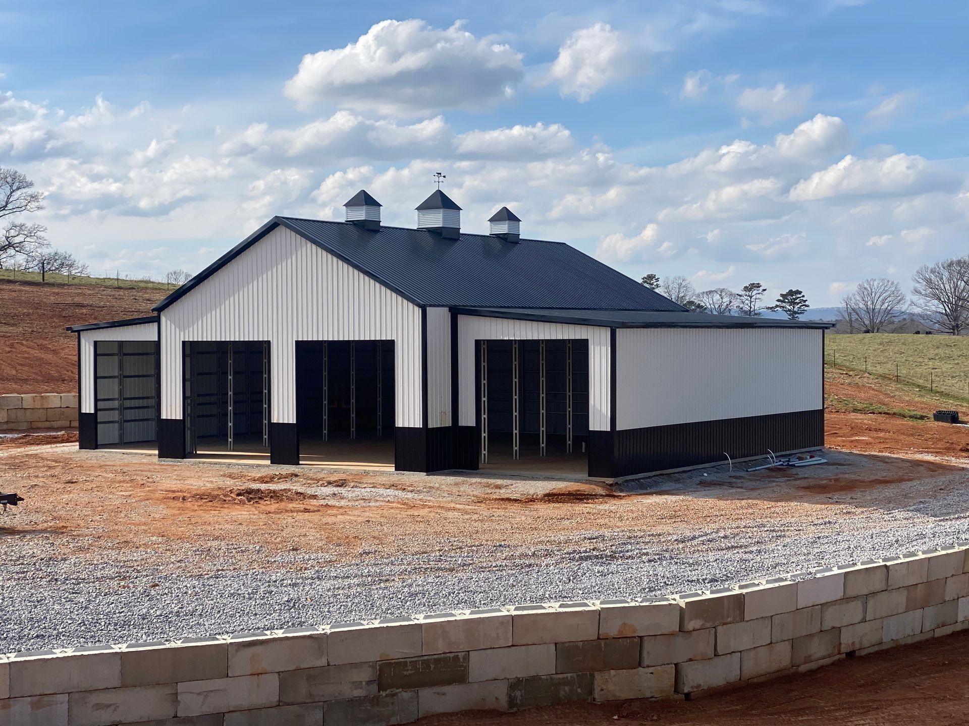 White and black barn-style building with open garage bays and a blue sky.