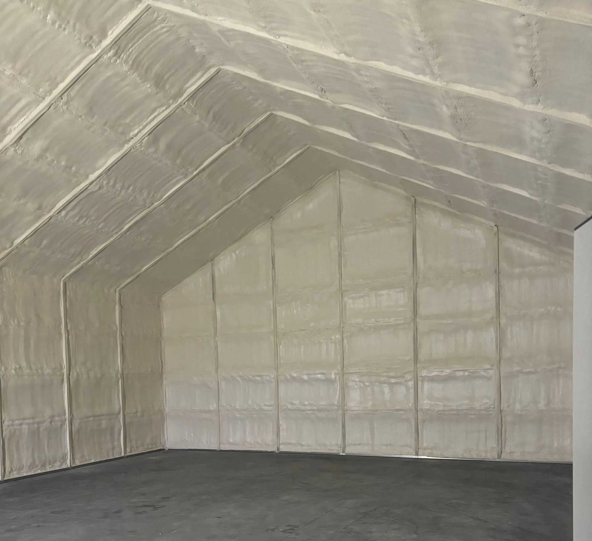 Interior view of a building with exposed spray foam insulation on walls and sloped ceiling; gray floor.