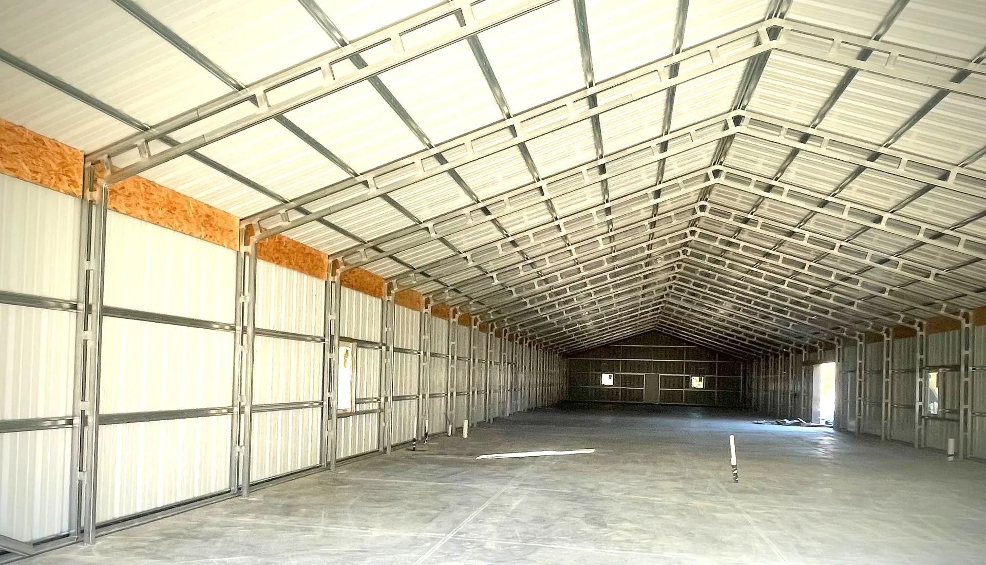 Interior of a large, empty metal building with a white roof and walls.