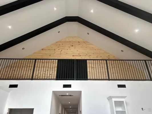 Interior view of a vaulted ceiling with exposed beams, a wood-paneled gable, and a black railing.