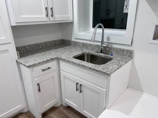 White cabinets and countertop with a sink, faucet, and window.
