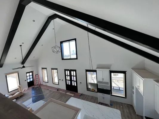 Interior of a newly renovated house with high ceilings and black beams, featuring white walls, windows, and black doors.