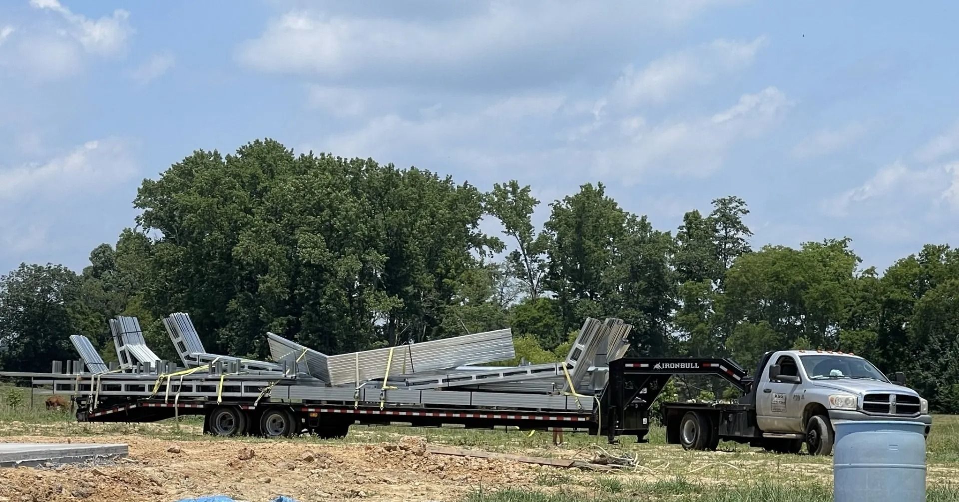 Truck with trailer loaded with metal building components on a construction site.