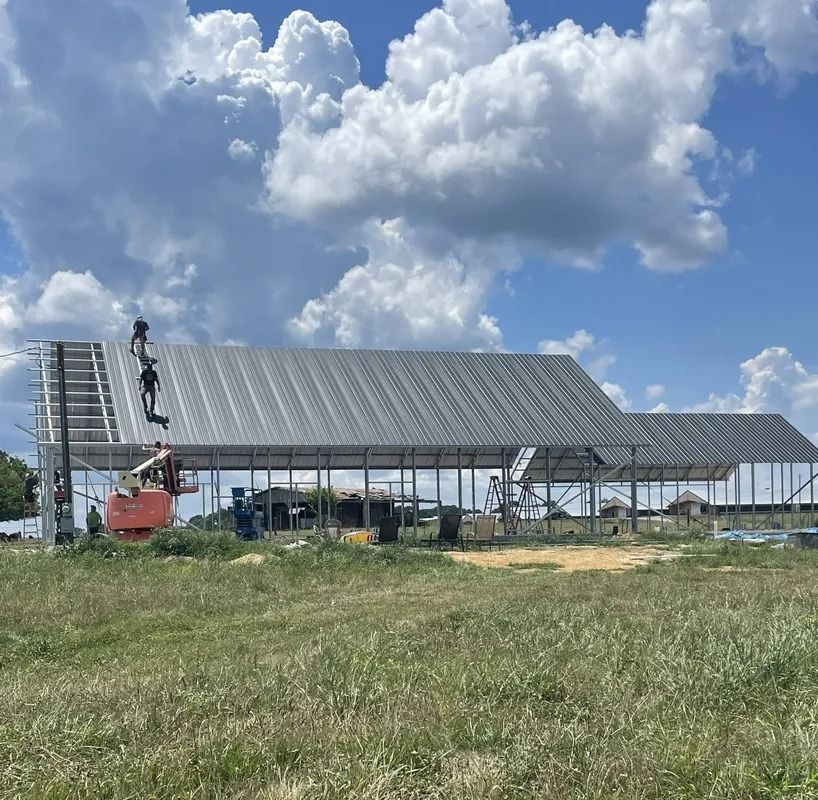 Construction workers on a partially-built metal roof, orange lift, blue sky, green field.