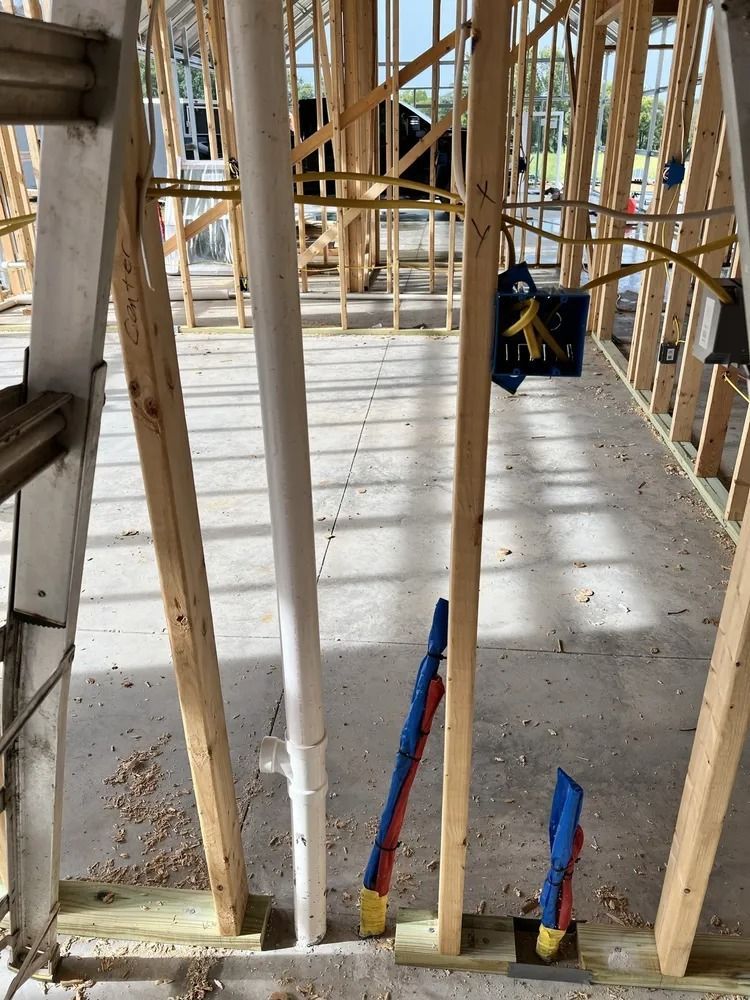 Interior framing of a building under construction, showing plumbing pipes and electrical wiring.