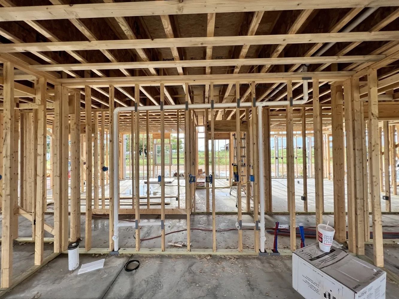 Wooden house under construction; interior view with framing, plumbing, and wiring visible.