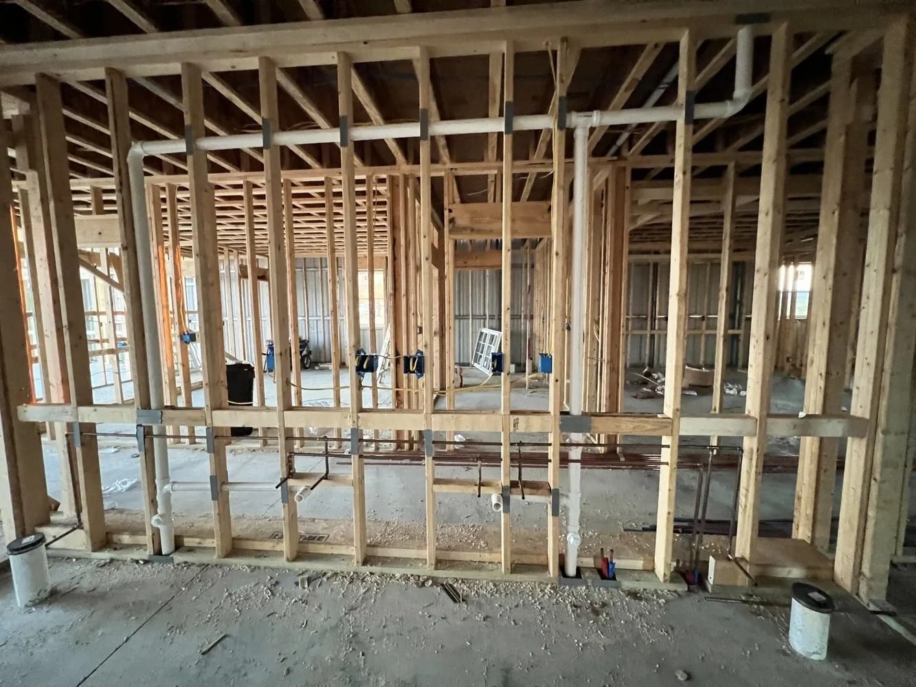 Interior house framing under construction with exposed wooden studs and plumbing.