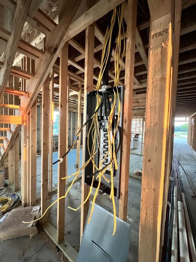 Electrical panel installed in the wooden framing of a building under construction, with exposed yellow wires.