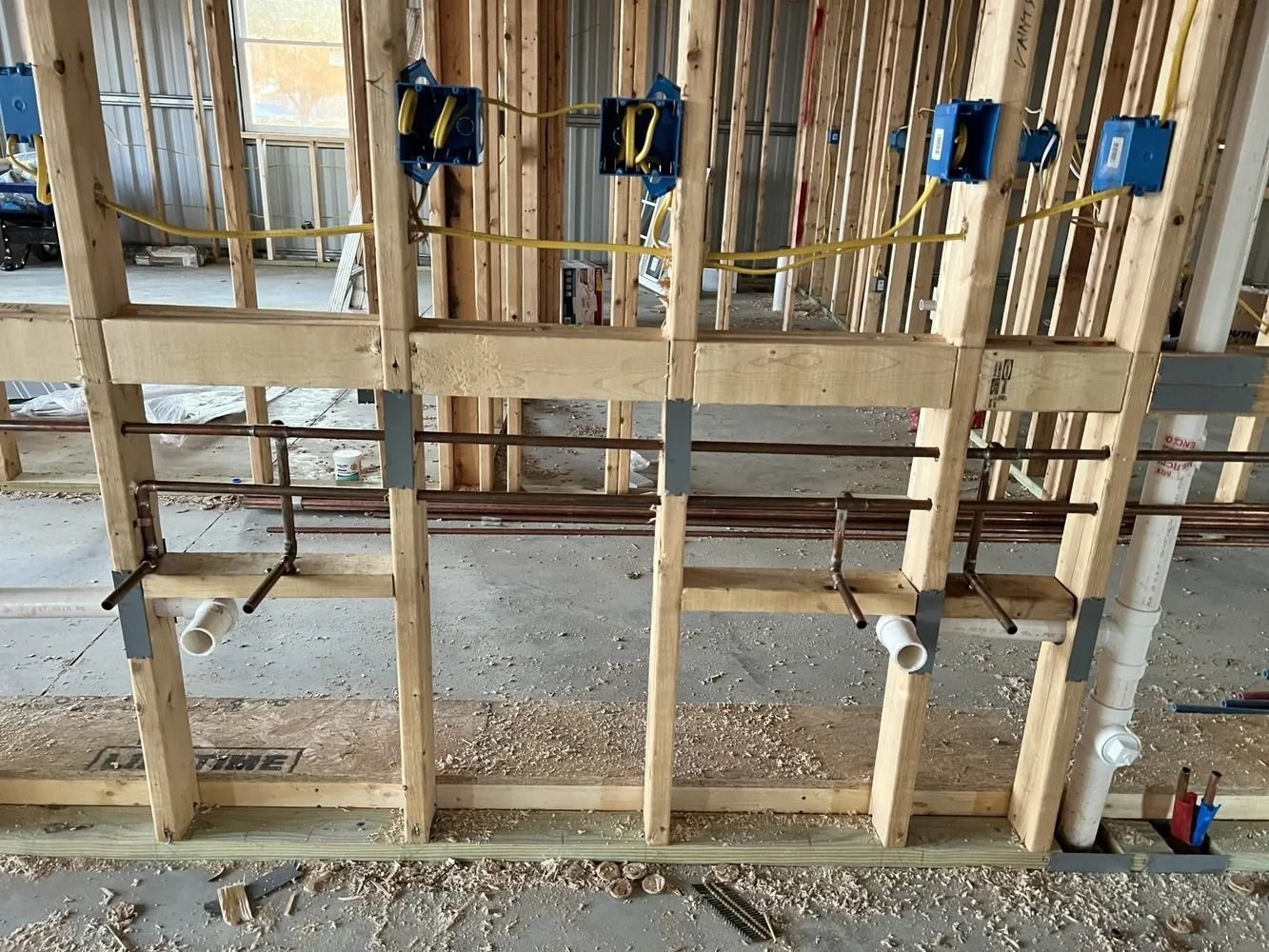 Wooden wall under construction with electrical boxes and plumbing pipes.