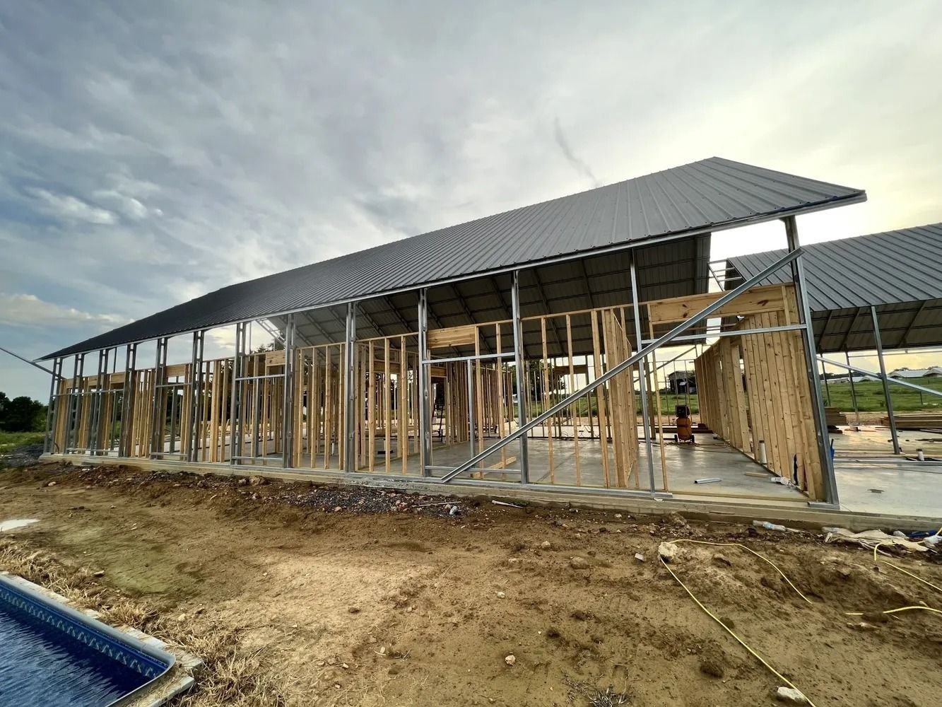 Building in progress with wood framing and gray metal roof under cloudy sky.
