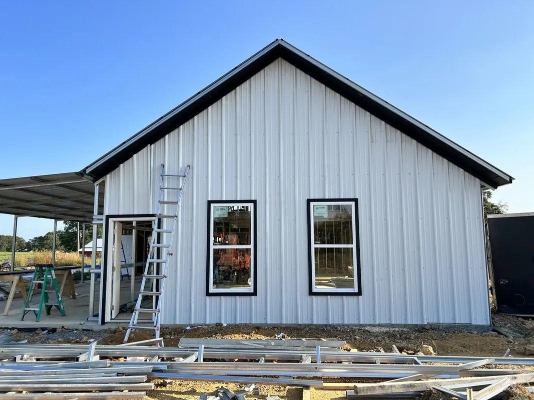 White-sided building under construction with two windows and a ladder leaning against it.
