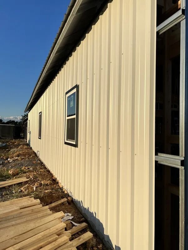 Beige metal-sided building with a few windows under construction; wood planks on the ground.