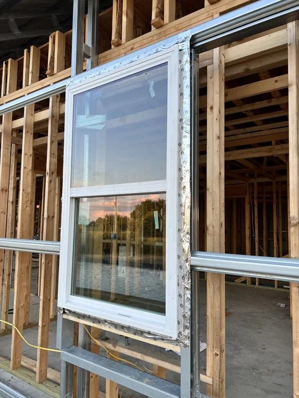 A window installed in the frame of a building under construction, with a reflective view of a body of water.
