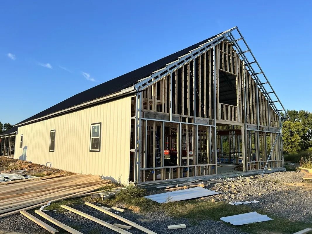 Barn under construction; wood and metal framing, blue sky.