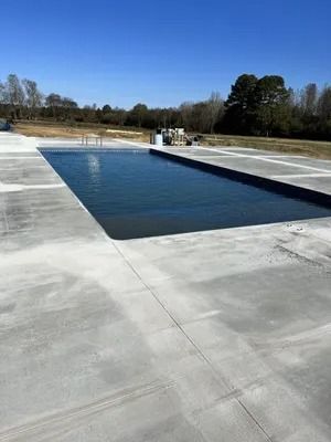 Rectangular pool with dark water, surrounded by light gray concrete, outdoors on a sunny day.