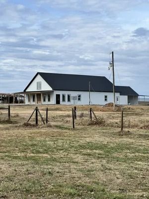 White farmhouse with black roof under cloudy sky, with small wooden fence in the foreground.