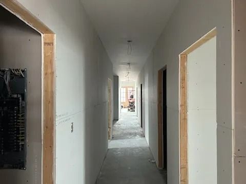 Narrow hallway under construction with unfinished walls, doorways, and electrical panel.