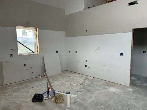 Interior room under construction; drywall installed, gray walls, concrete floor.