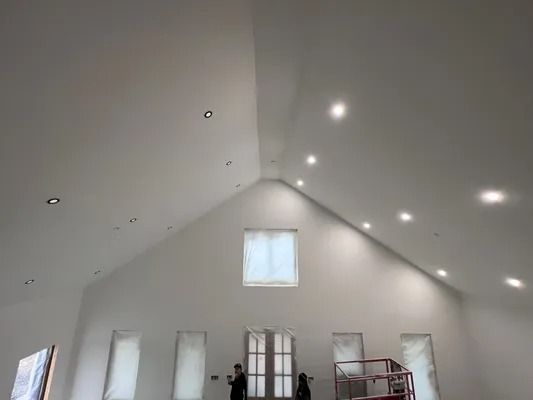 High-ceilinged white room with recessed lights, windows covered with protective sheeting, and two figures.
