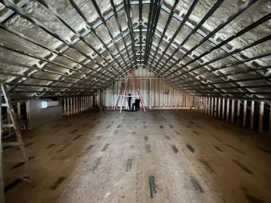 Interior of an unfinished attic with wood flooring, exposed beams, and insulation.