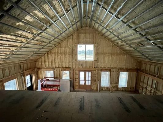 Interior of a building under construction with exposed wooden framing, windows, and insulation.