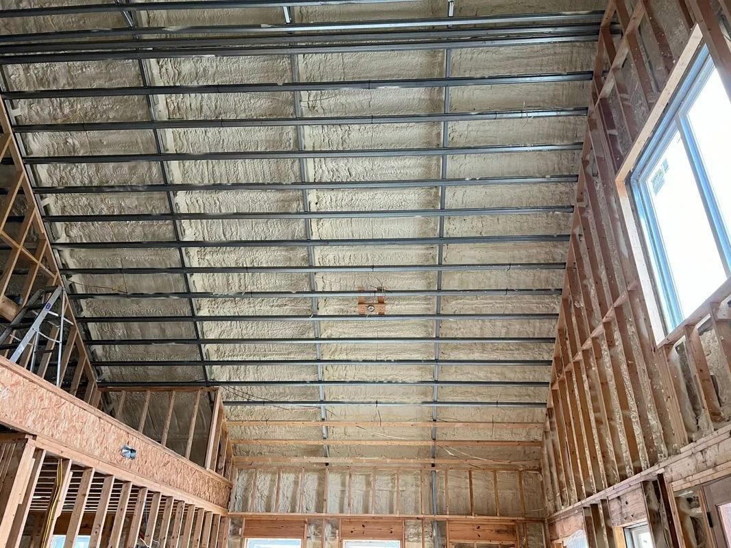 Interior view of a building under construction, with exposed wooden beams and spray foam insulation.