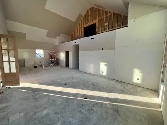 Interior construction site: large room with unfinished walls, exposed framing, and concrete floor.