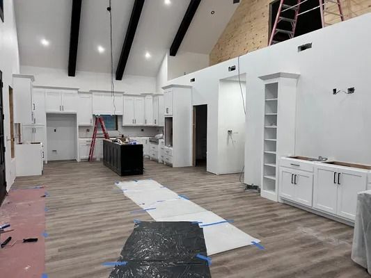 Spacious kitchen with white cabinets, black island, and exposed beams. Construction in progress.