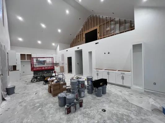 Interior room under construction; white walls, paint cans, lift, exposed wood, cabinets.