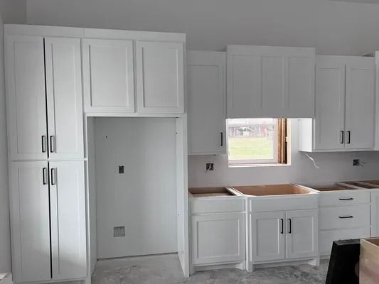 White kitchen cabinets with black handles, unfinished countertop, and open refrigerator space.