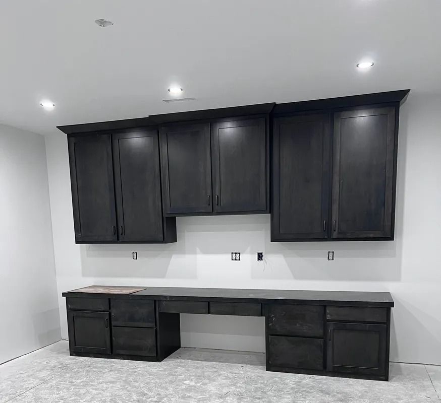 Dark gray cabinets above a matching desk in a room with white walls and recessed lights.