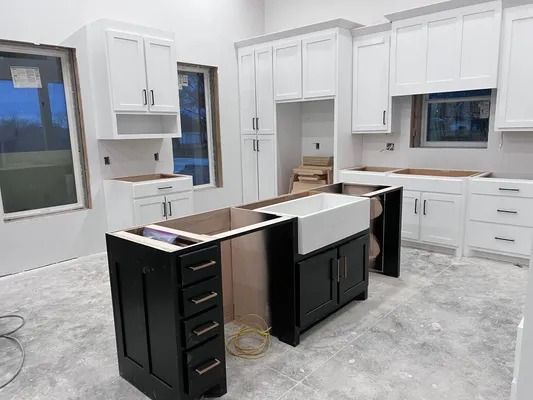 Kitchen under construction with white cabinets, black island, and a farmhouse sink.