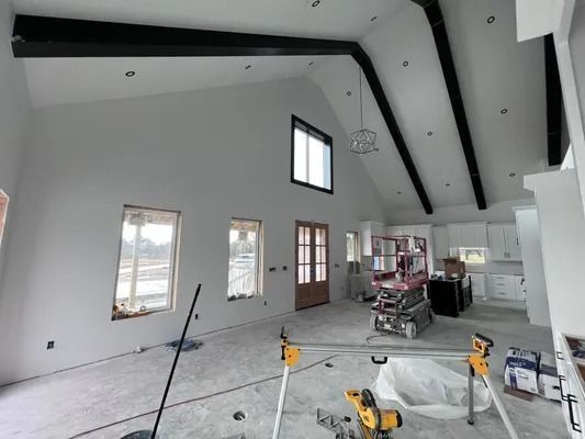 Interior of a house under construction; white walls, black beams, windows, and construction equipment.