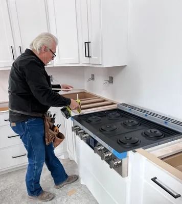 Man installing a countertop above a white range stove in a kitchen.