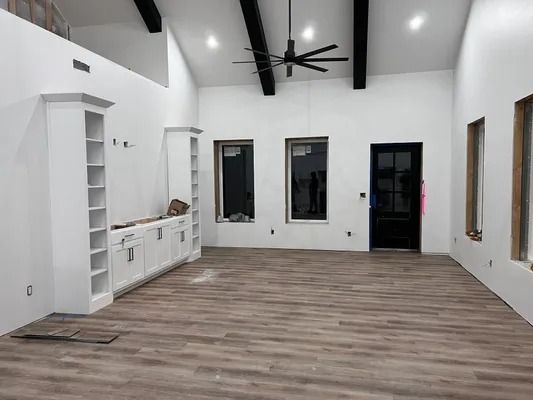 Empty white room with wood-look flooring, built-in cabinets, black door and trim, windows, and ceiling beams.