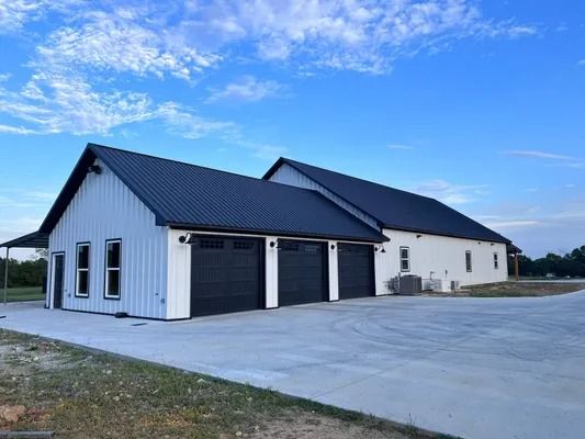 Modern building with three garage doors, light and dark exterior colors, and a concrete driveway under a blue sky.