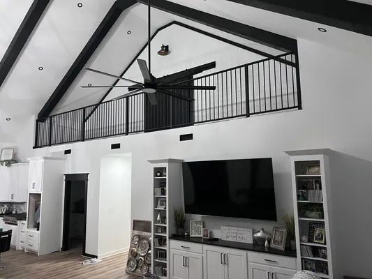 Interior with a loft. White walls, black trim, railing and ceiling fan. Television above a cabinet.