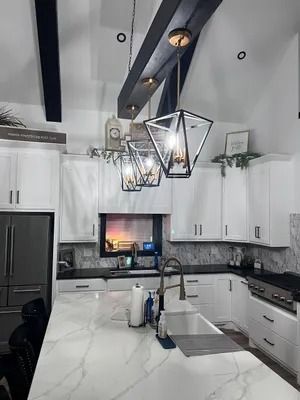 White kitchen with marble countertops, black accents, and geometric pendant lights.