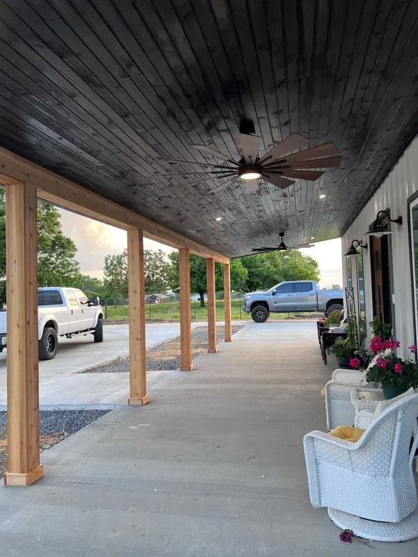 Covered porch with black ceiling, wood posts, and trucks parked in front.