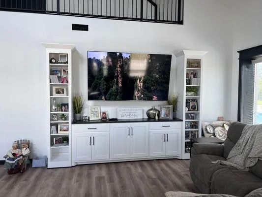 Living room with white built-in entertainment center, TV, and bookcases. Gray sofa and wooden floor.