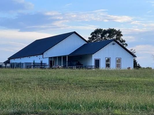 White barn with a black roof and a covered porch, in a grassy field under a cloudy sky.