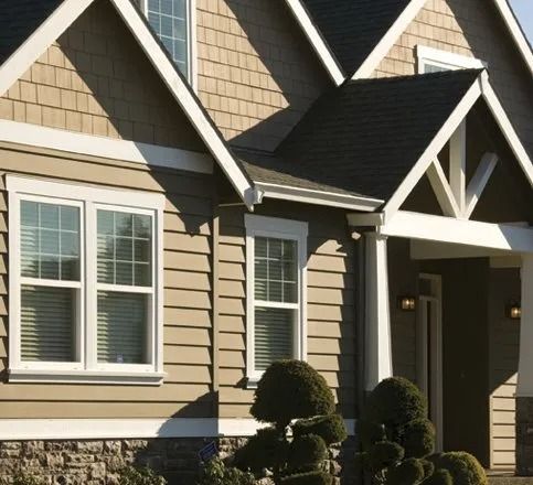 Tan house exterior with white trim, windows, and dark roof.