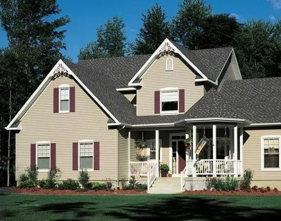 Beige two-story house with dark roof and maroon shutters; front porch. Trees in background.