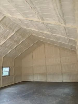 Interior view of a building with spray foam insulation on the walls and ceiling. The walls are white and the floor is dark gray.