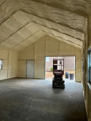 Interior of a building insulated with yellow foam. A lift sits near an open garage door.
