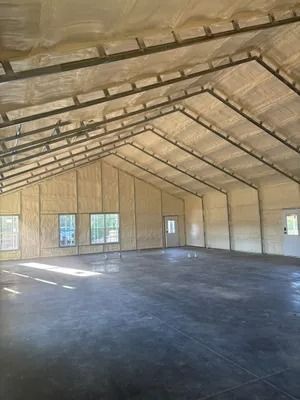 Interior of a large, newly constructed building with spray foam insulation. Concrete floor, windows and doors visible.
