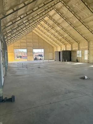Interior of a large concrete building, angled roof with beige insulation, empty space, large open doors.