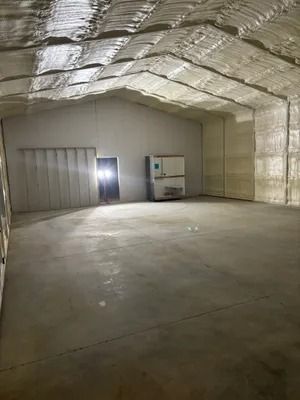 Empty warehouse interior with spray foam insulation, concrete floor, and doorway.