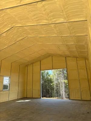 Interior view of a building with yellow spray foam insulation on walls and ceiling; open doorway reveals trees.