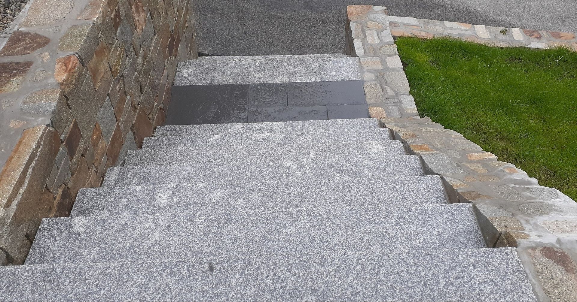 A set of stairs made of granite next to a stone wall.